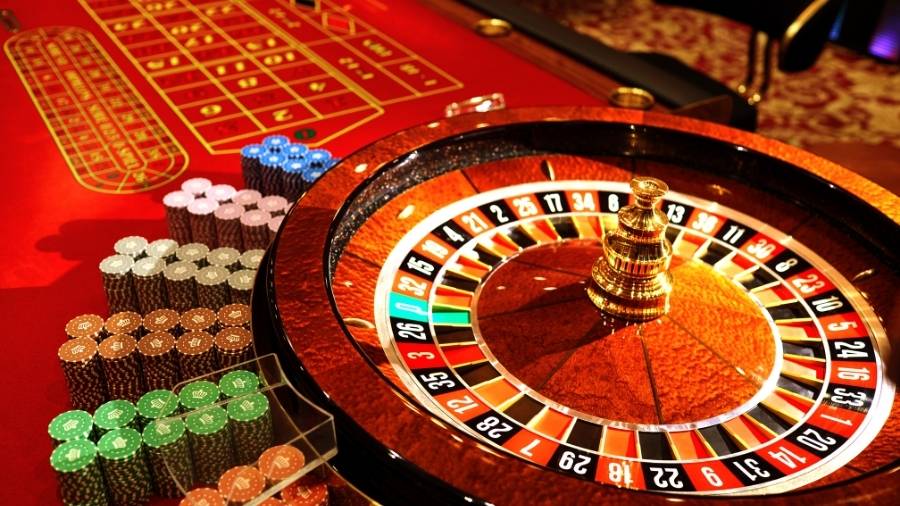 Roulette wheel with colorful chips in a luxury casino setting, featuring red and gold tones under bright lights