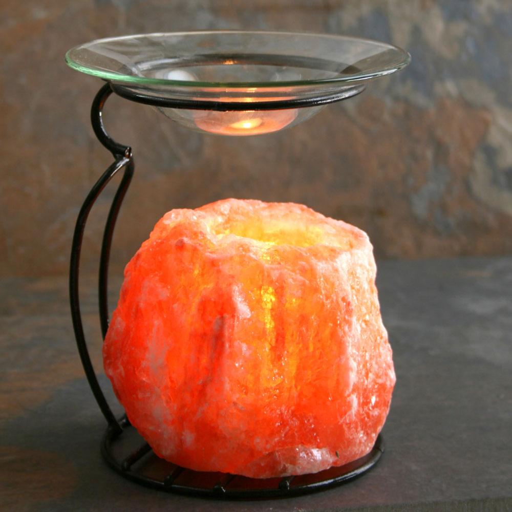 Salt lamp oil burner with a glowing orange Himalayan salt base and a glass dish on a black metal stand.