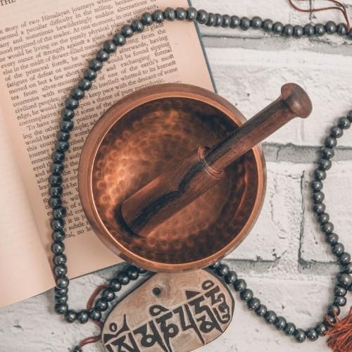 brass singing bowl with beater and necklace in backdrop